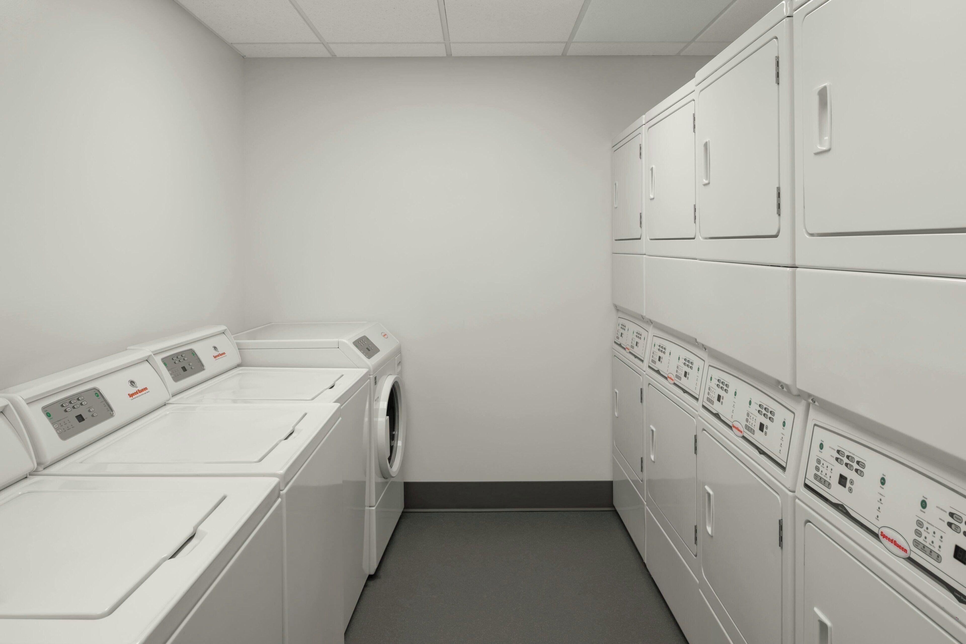 A laundry room with stacked washing machines and dryers, a grey floor, and white walls.