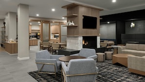 A modern lounge area with a fireplace, seating arrangements, and a kitchen in the background. - Residence Inn By Marriott Eagle Boise (Eagle)