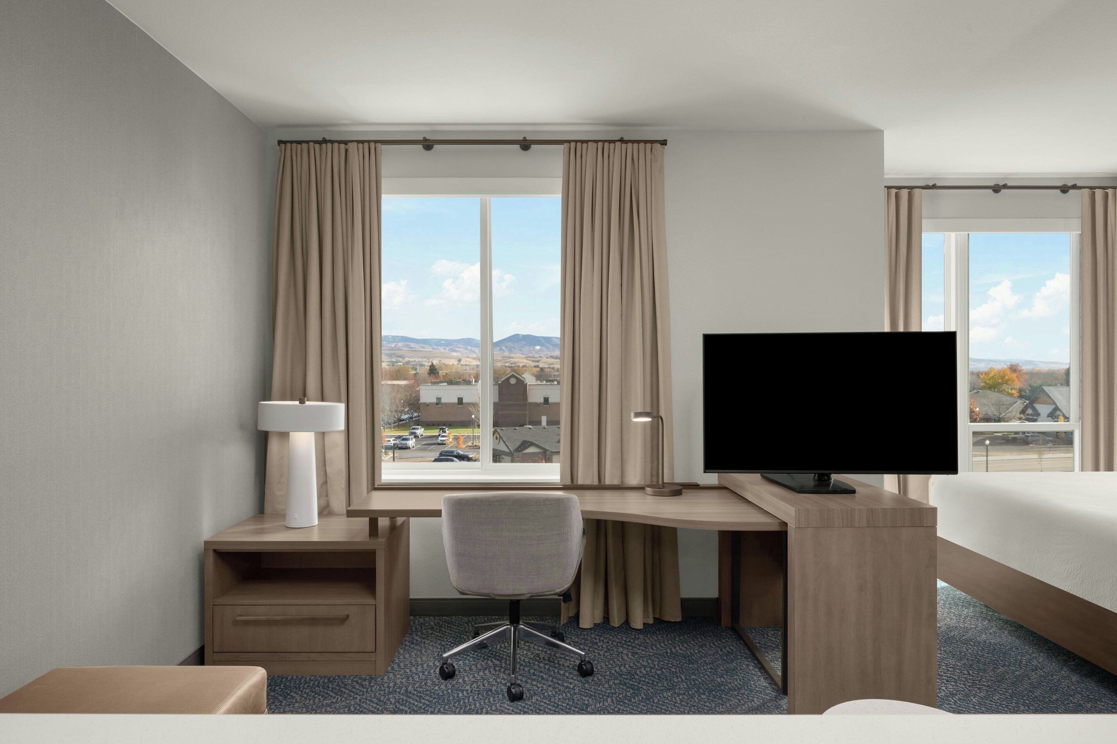 Une chambre d’hôtel équipée d’un bureau, d’une chaise, d’une télévision et offrant une vue sur le paysage urbain.