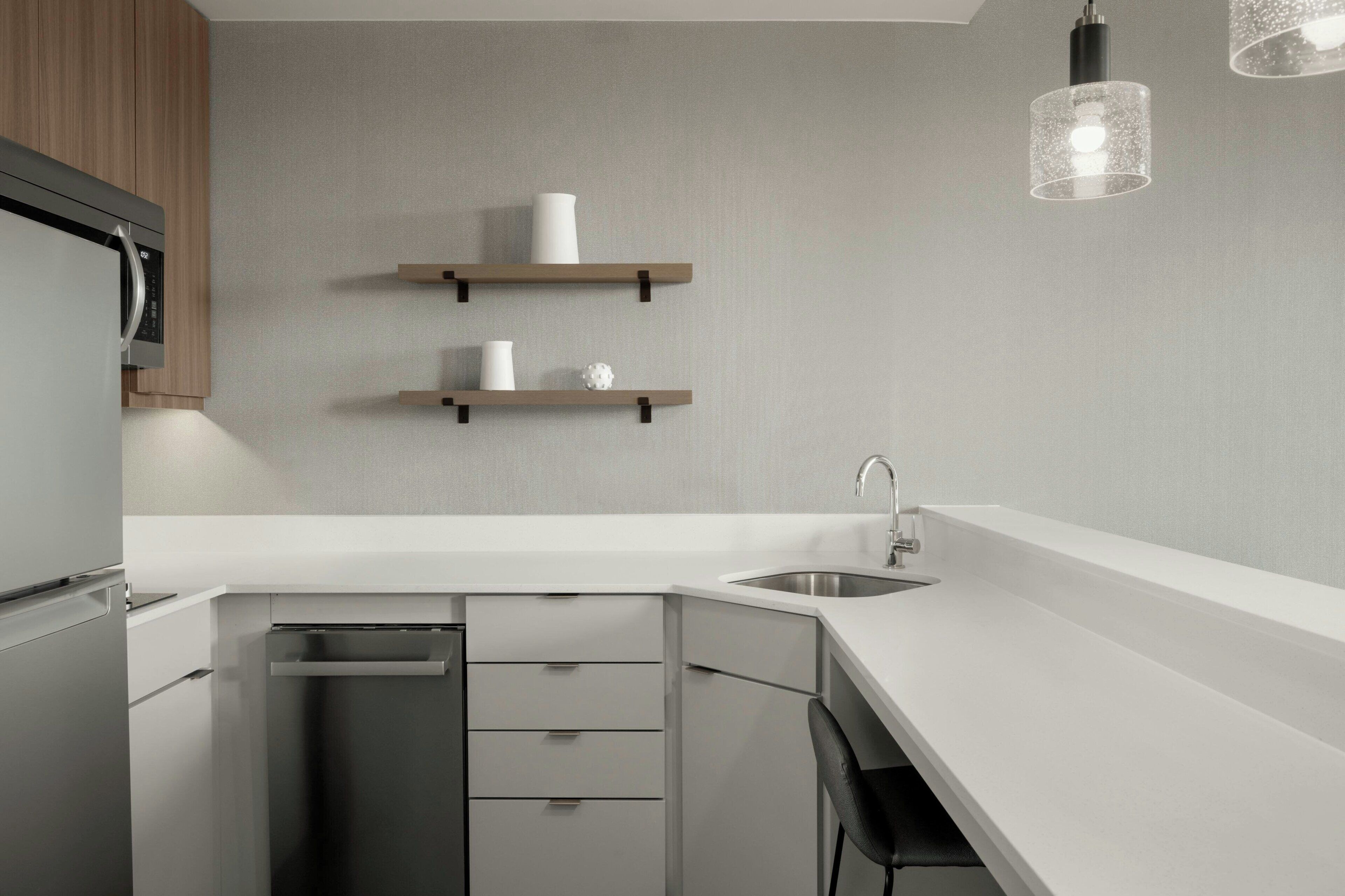 A modern kitchen with white countertops, stainless steel appliances, and wooden shelves.