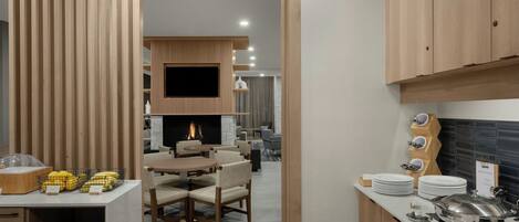 A modern kitchen with wooden cabinets, a dining area with a fireplace, and a buffet setup with plates and bowls.