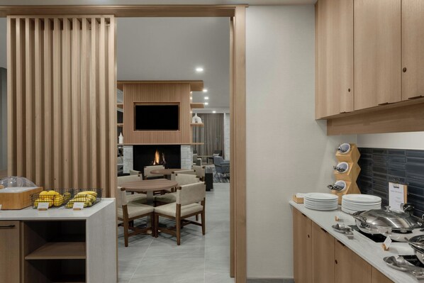 A modern kitchen with wooden cabinets, a dining area with a fireplace, and a buffet setup with plates and bowls.