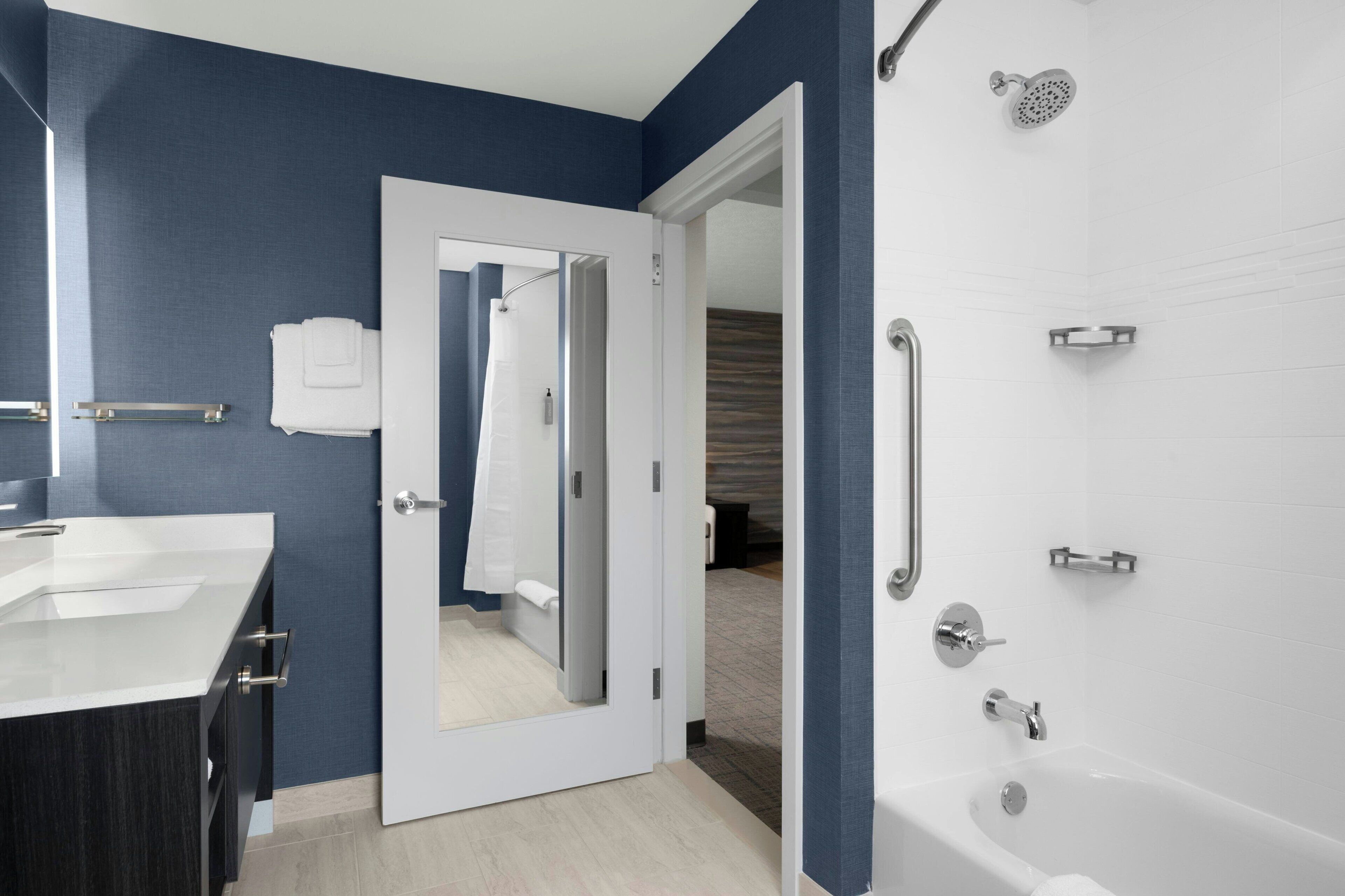 A modern bathroom with a white bathtub, a large mirror, and a vanity with a sink.