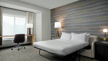 Habitación de hotel con cama, escritorio, silla, lámpara y vistas al exterior.