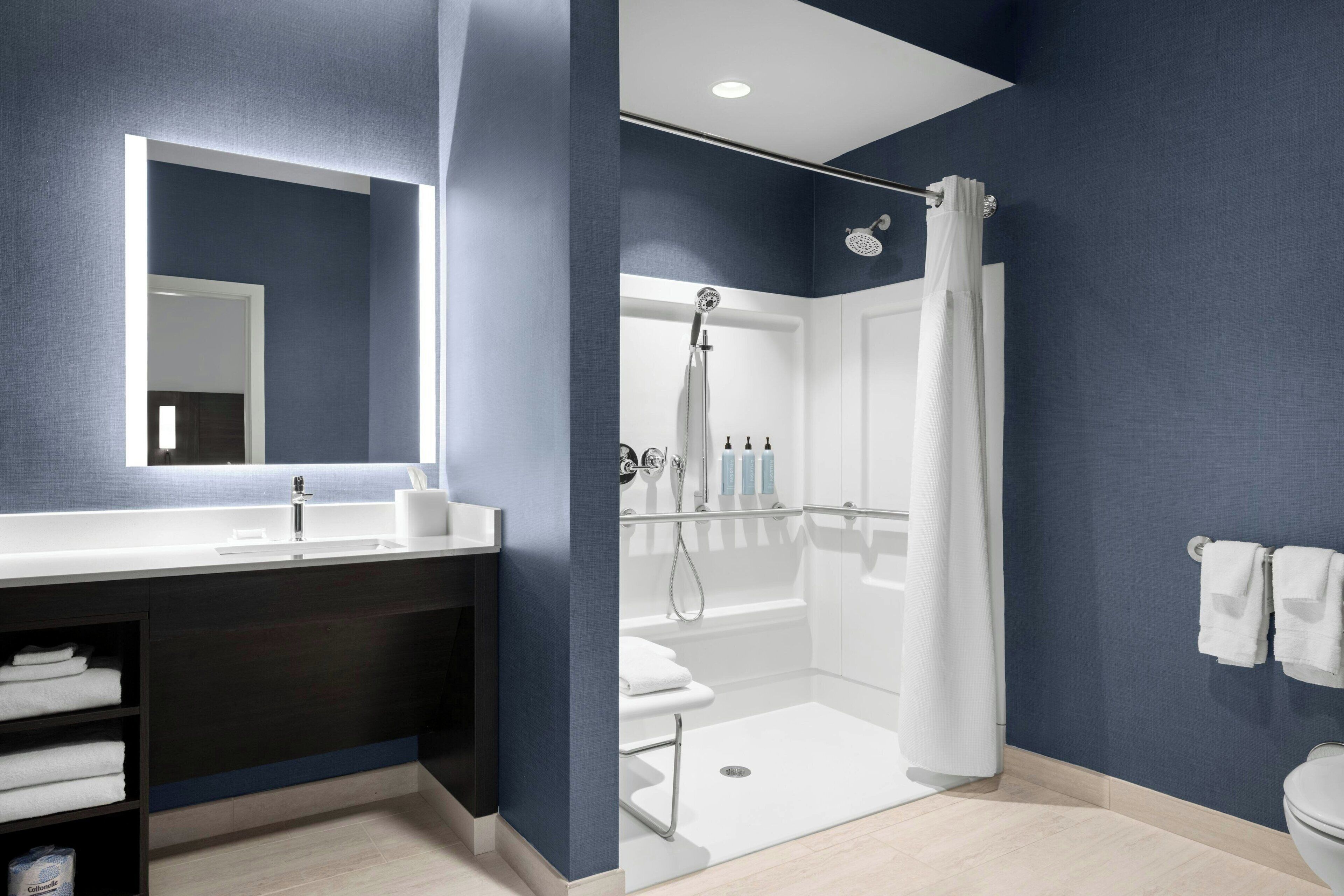 A modern bathroom with a large mirror, white sink, and a walk-in shower.