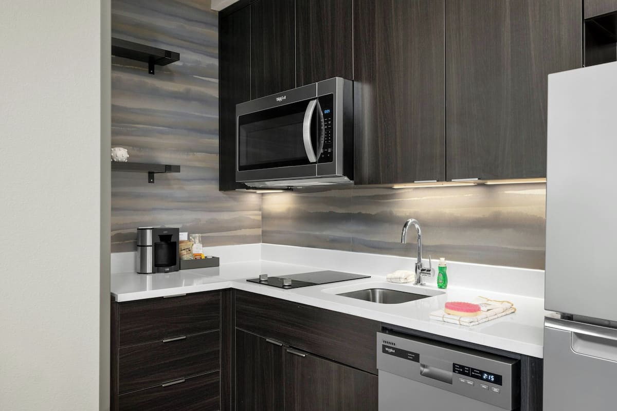 Una cocina moderna con armarios de madera oscura, un microondas de acero inoxidable, una cafetera y un lavavajillas.