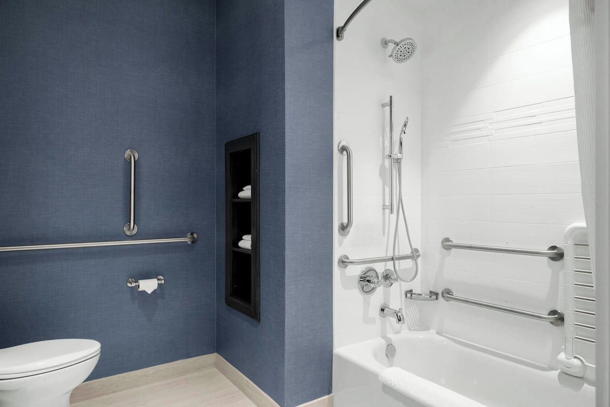 Un baño con inodoro, lavamanos y zona de ducha con barras de apoyo.