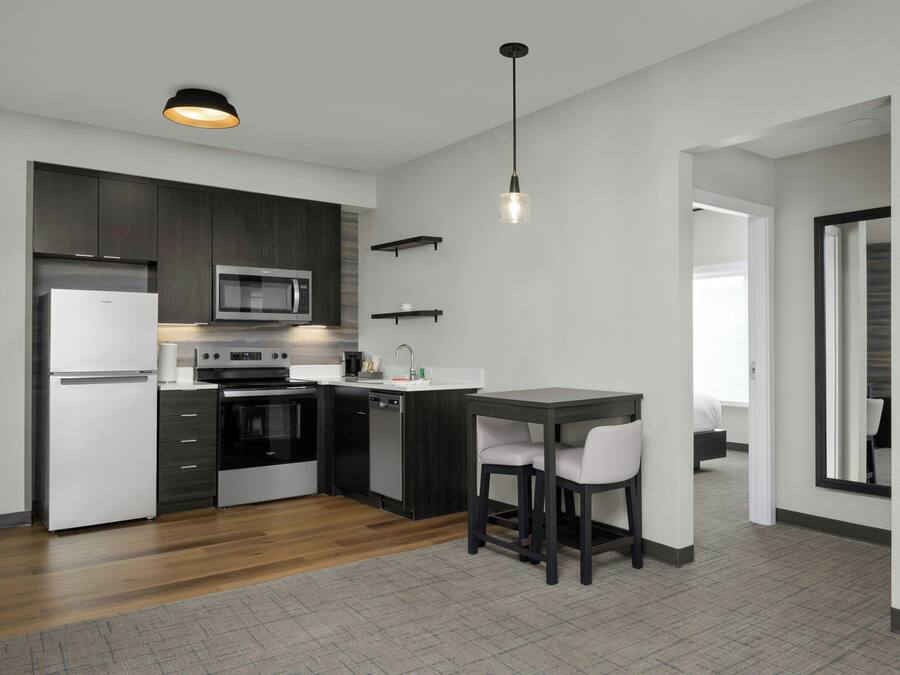 A modern kitchen with dark cabinetry, a microwave, a refrigerator, and a bar area with two stools.