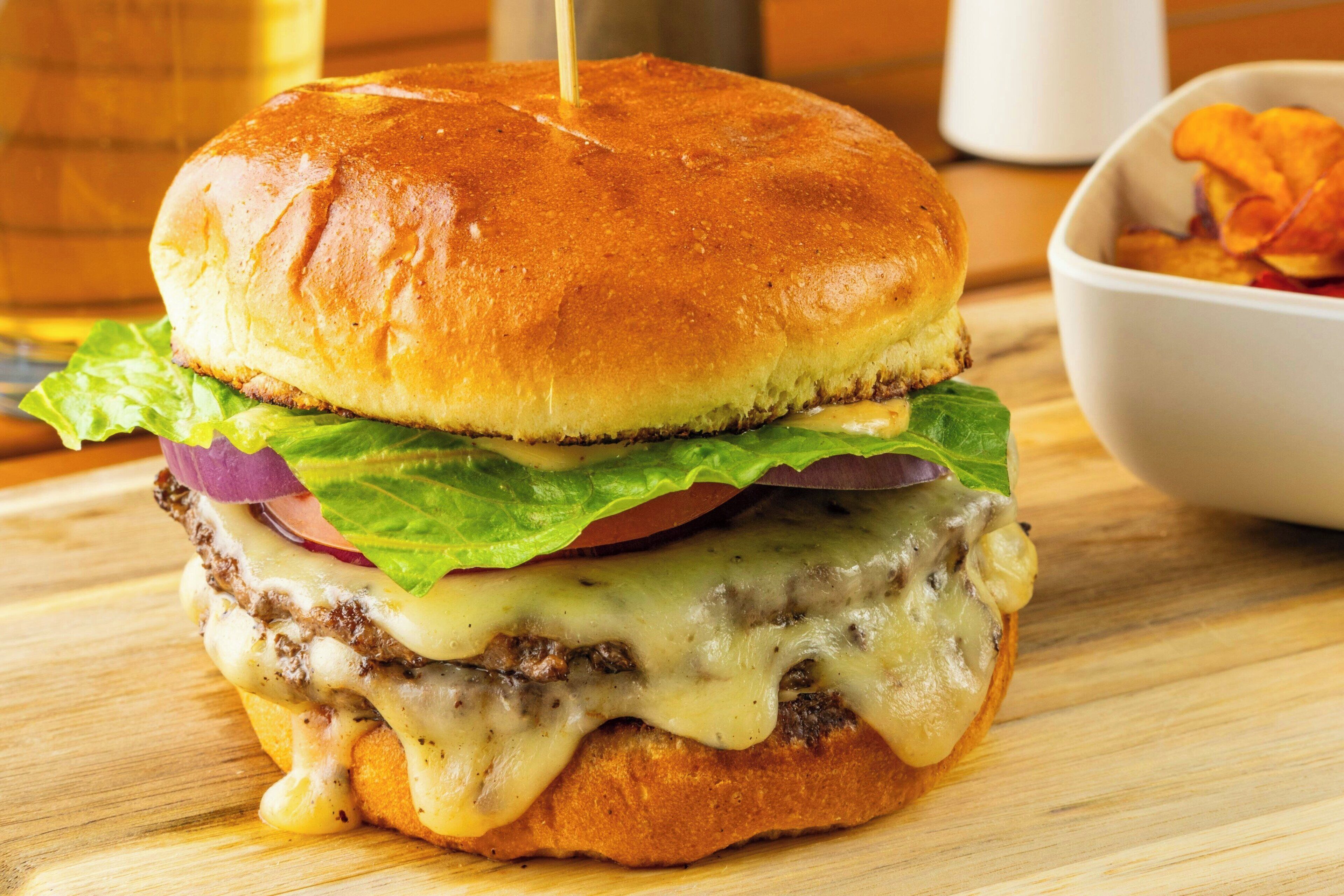 Un hamburger servi dans un pain grillé, avec de la laitue, des tomates et du fromage.