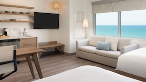 A modern hotel room with a kitchen area, a sofa, a bed, and a large window with a view of the sea. - Element by Marriott Melbourne Oceanfront (Indialantic)