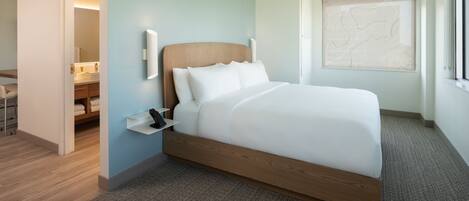 A modern hotel room with a wooden bed, a bedside table, and a large window with a view.
