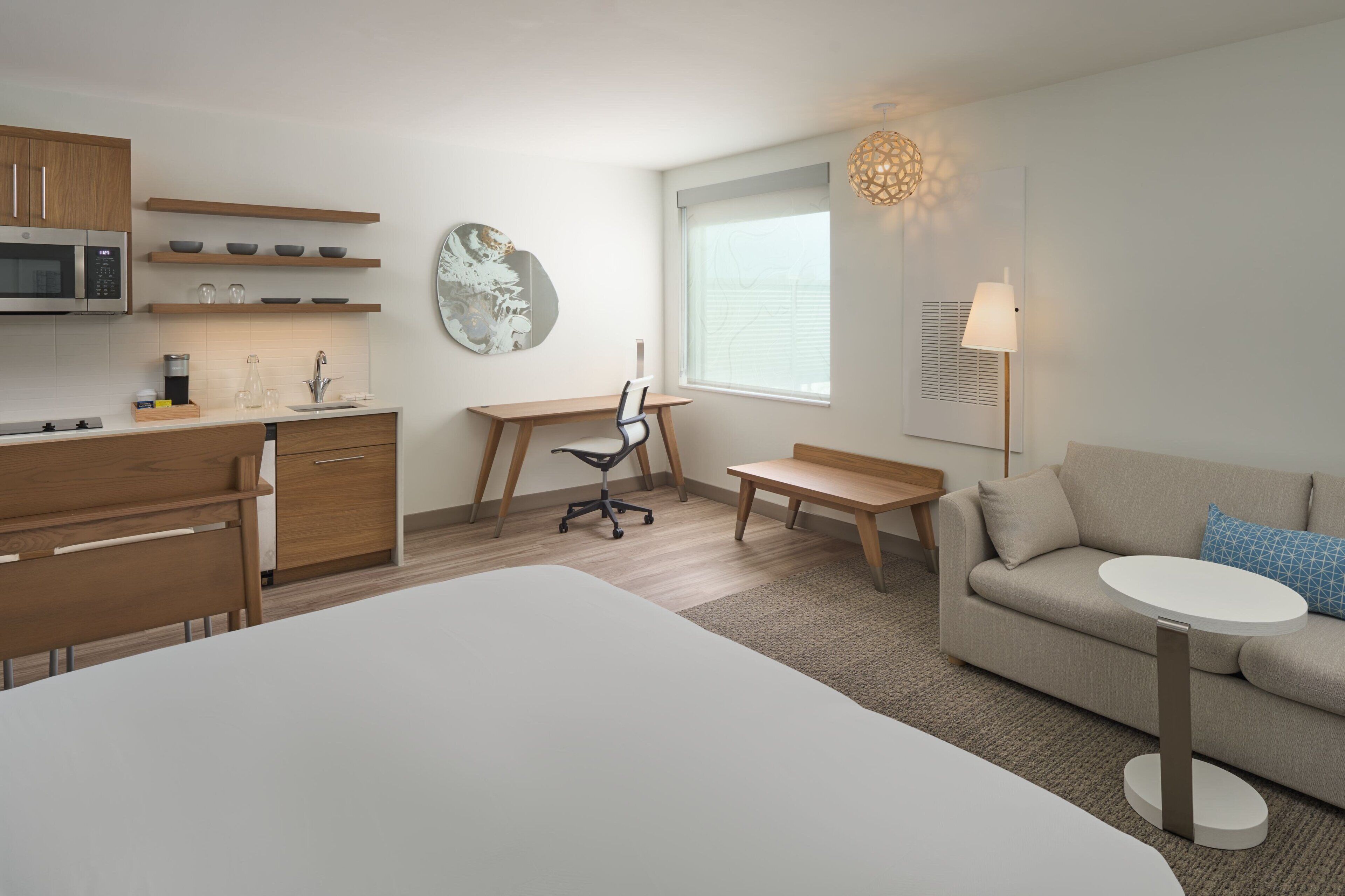 A modern, well-lit room with a kitchenette, a dining area, a sofa, and a bed.