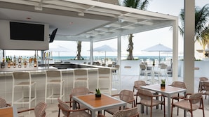 An outdoor bar area with wicker chairs and tables, a TV mounted on the wall, and a view of the ocean. - Element by Marriott Melbourne Oceanfront (Indialantic)
