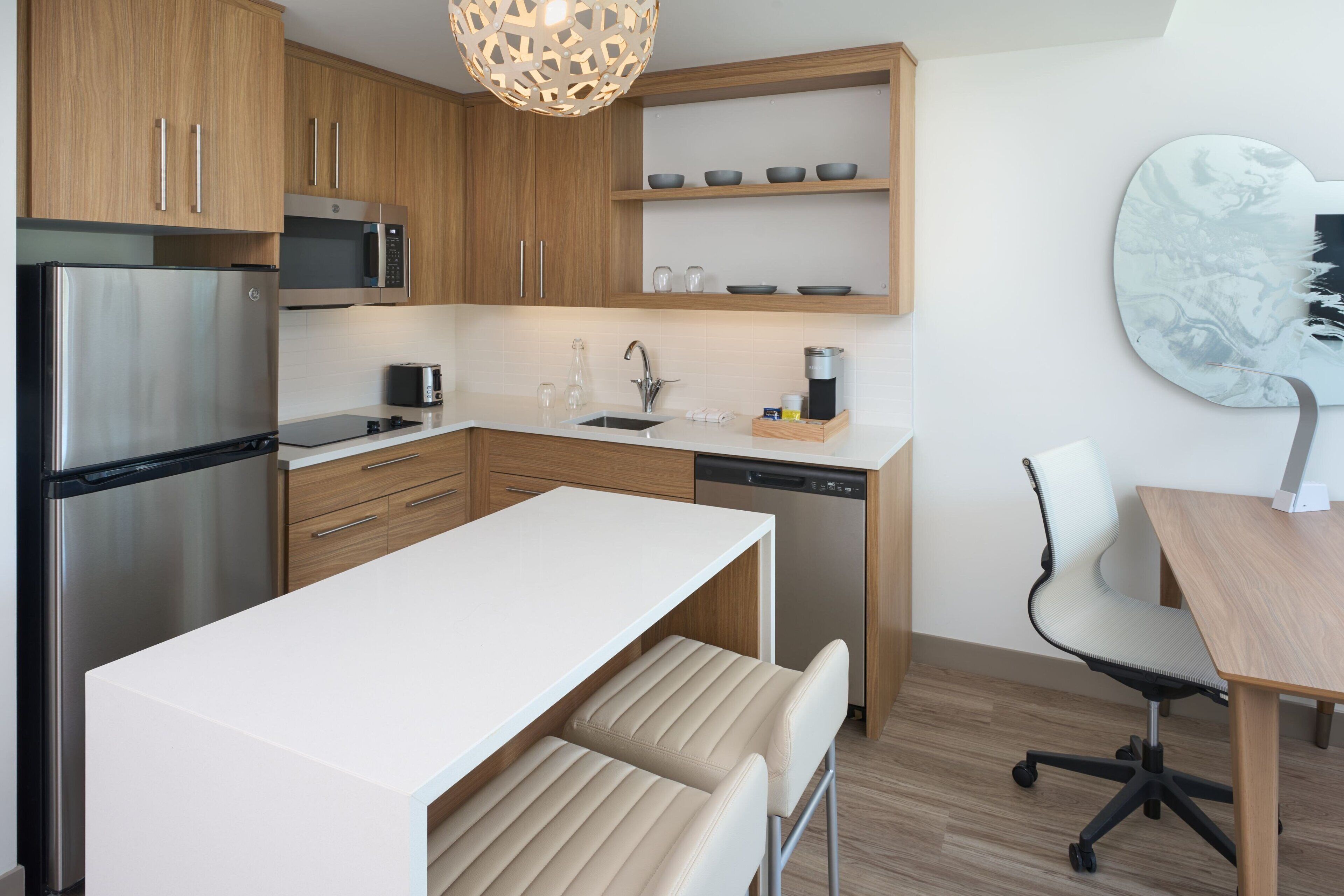 Een moderne keuken met houten kasten, roestvrijstalen apparatuur, een wit aanrecht en een eethoek met een houten tafel en stoelen.