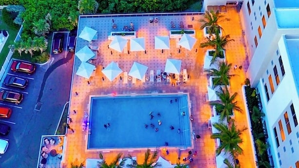 An aerial view of a hotel with a rooftop pool surrounded by palm trees and umbrellas, overlooking a beach. - Element by Marriott Melbourne Oceanfront (Indialantic)