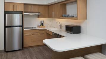A modern kitchen with wooden cabinets, a stainless steel refrigerator, a microwave, and a white countertop.
