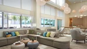 A modern hotel lobby with a large sectional sofa, round coffee tables, and contemporary lighting fixtures. - Element by Marriott Melbourne Oceanfront (Indialantic)