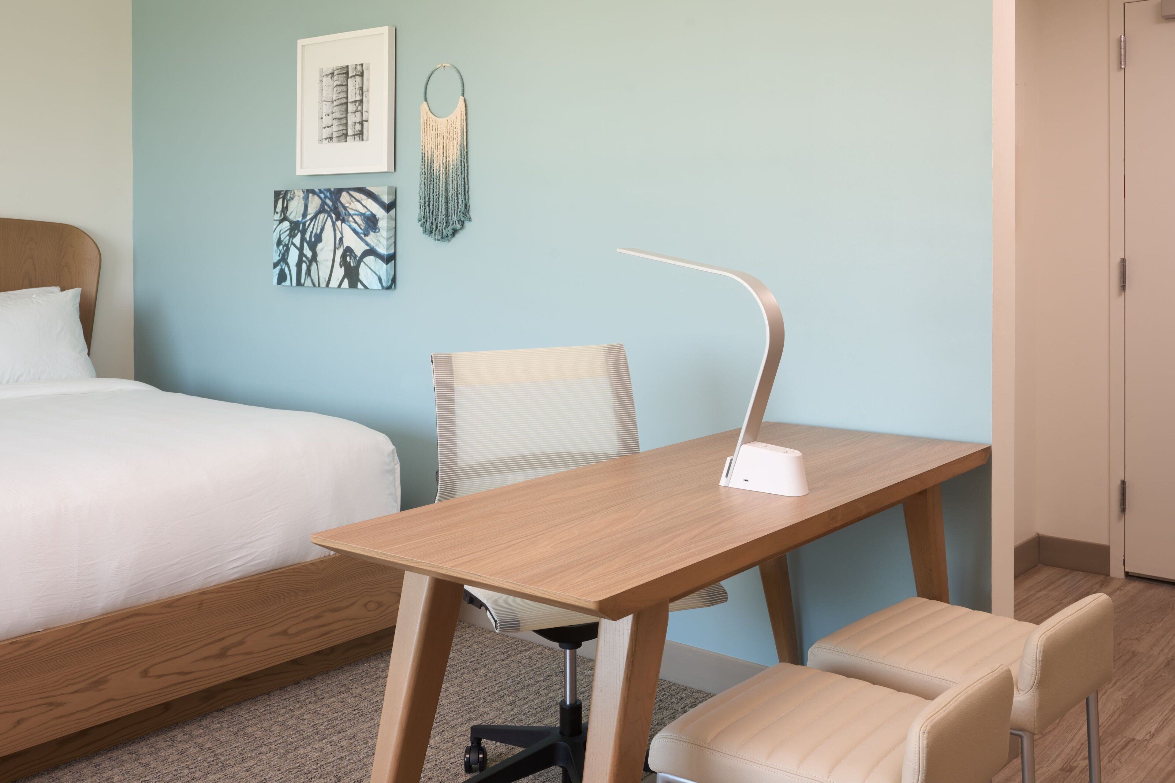 Una habitación de hotel con una cama, un escritorio con una silla y una pared decorada con obras de arte.