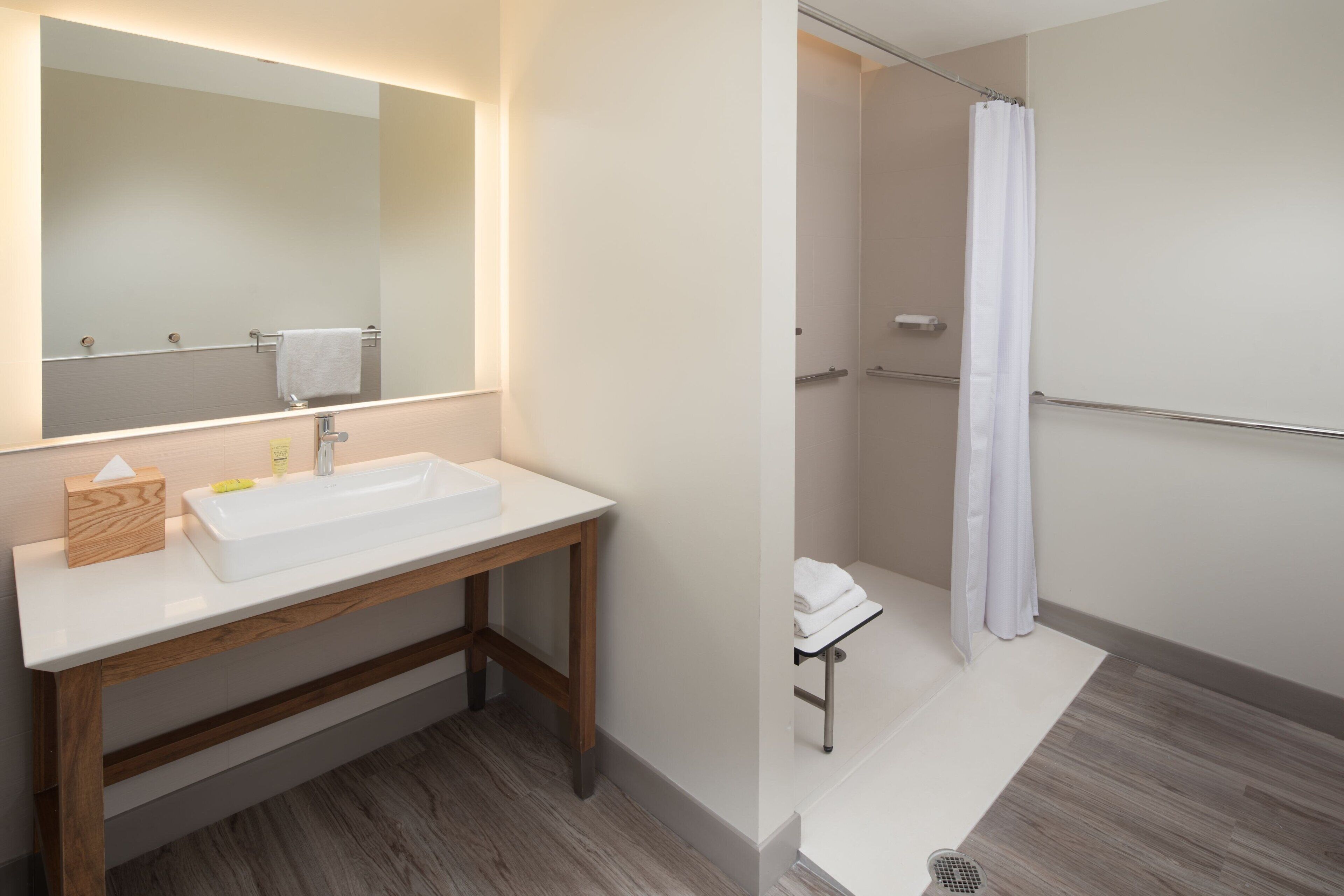 Une salle de bain avec un meuble-lavabo en bois, un grand miroir et un espace douche séparé par un rideau.