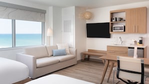 A modern hotel room with a large window, a sofa, a bed, a desk, a chair, and a kitchenette. - Element by Marriott Melbourne Oceanfront (Indialantic)
