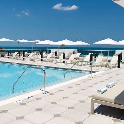 A poolside area with lounge chairs and umbrellas, a clear blue sky, and a view of the ocean.