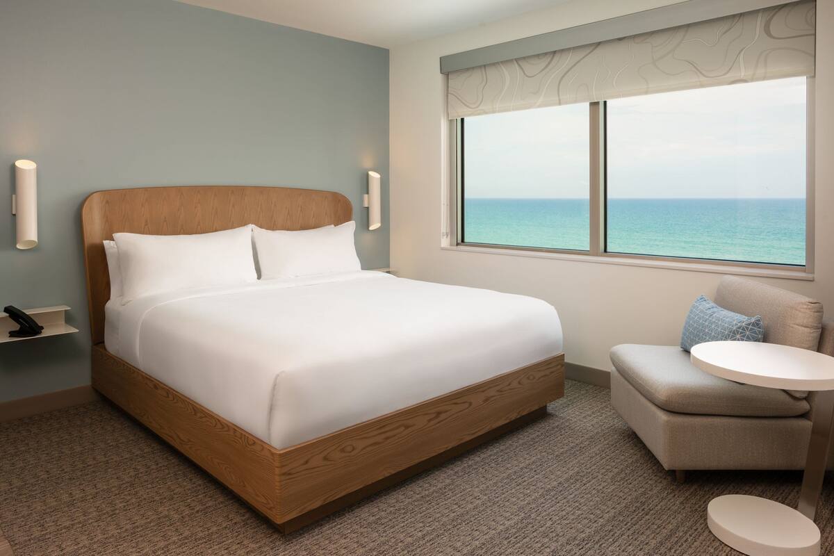 A hotel room with a wooden bed, a small round table, and a view of the sea.