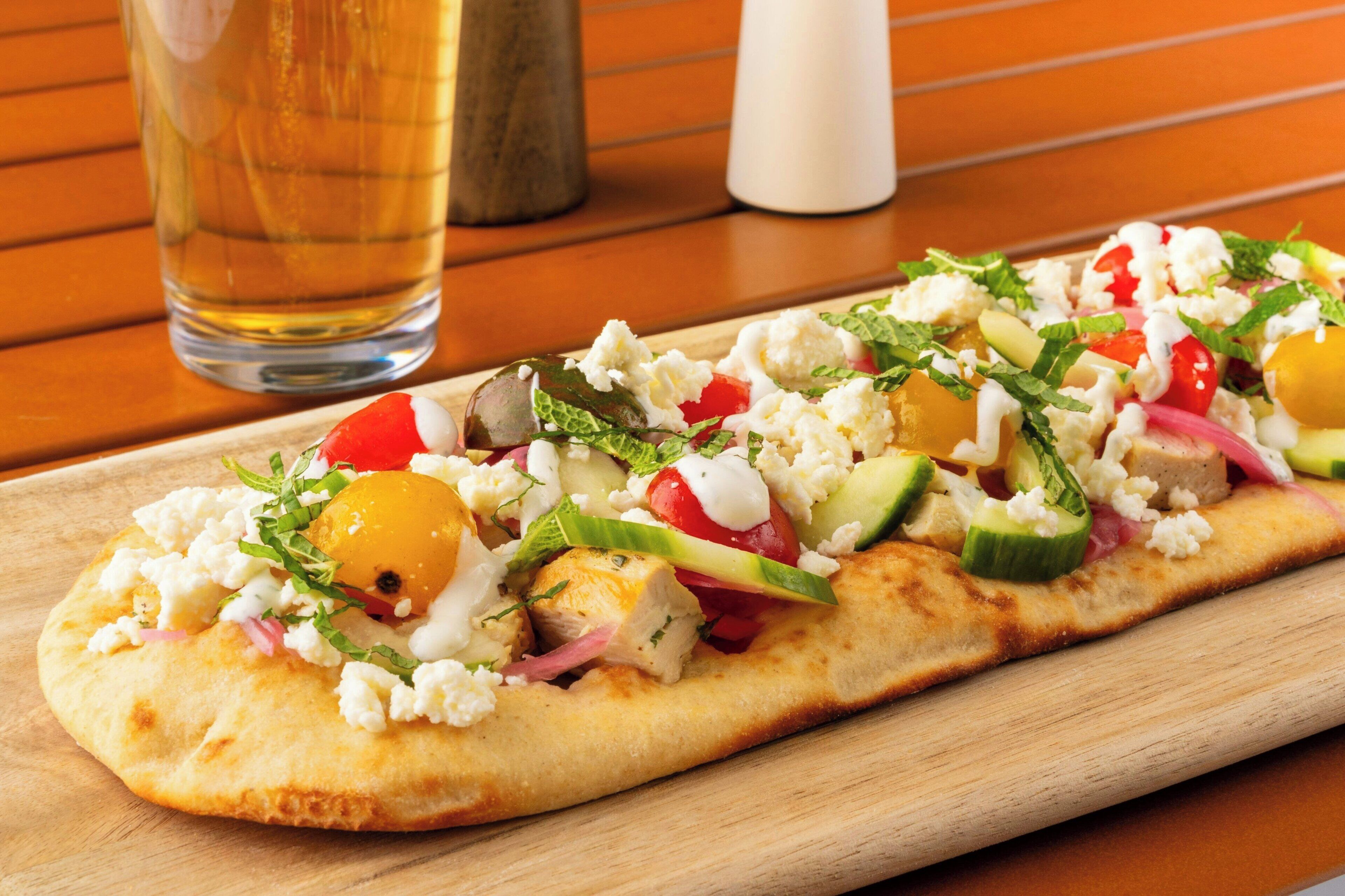 Une galette garnie de légumes et de fromage feta, servie sur une planche en bois.