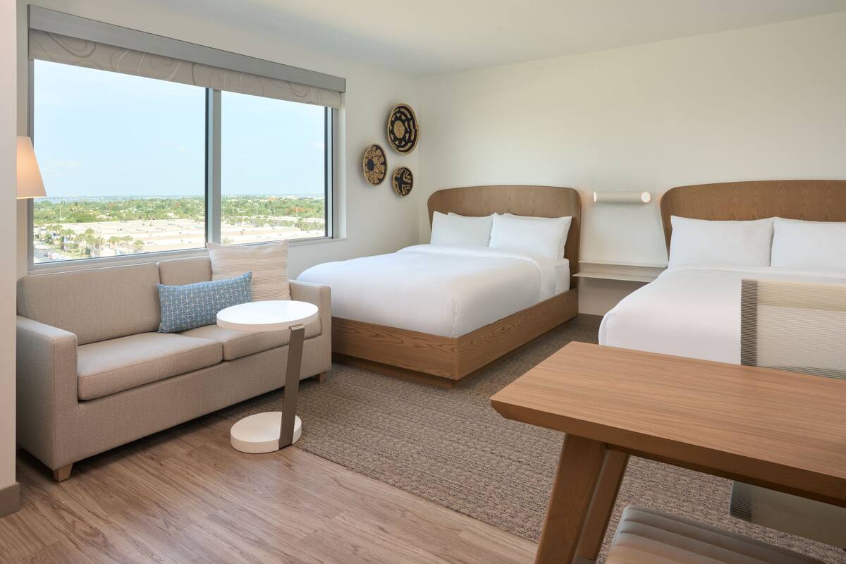 A hotel room with two beds, a sofa, a round table, and a view of the city.