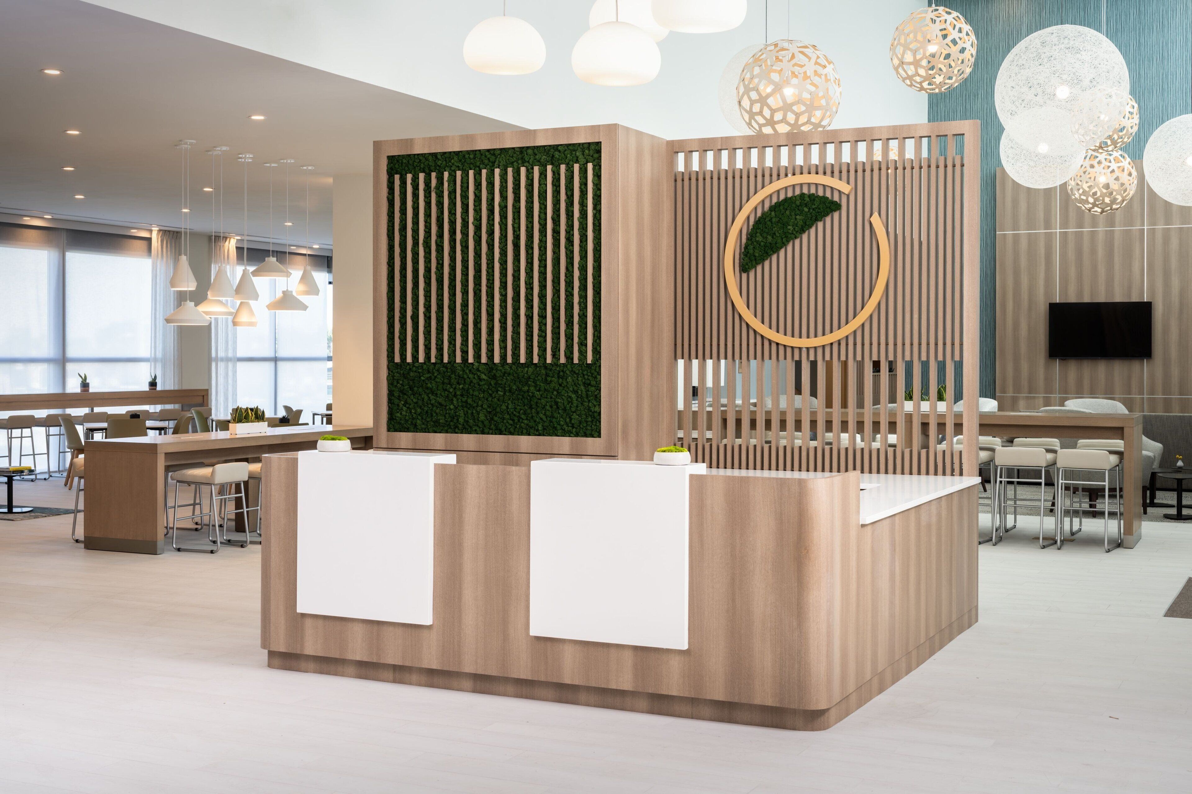 Un comptoir d’accueil moderne avec un revêtement en bois, un jardin vertical verdoyant et un élément décoratif circulaire.