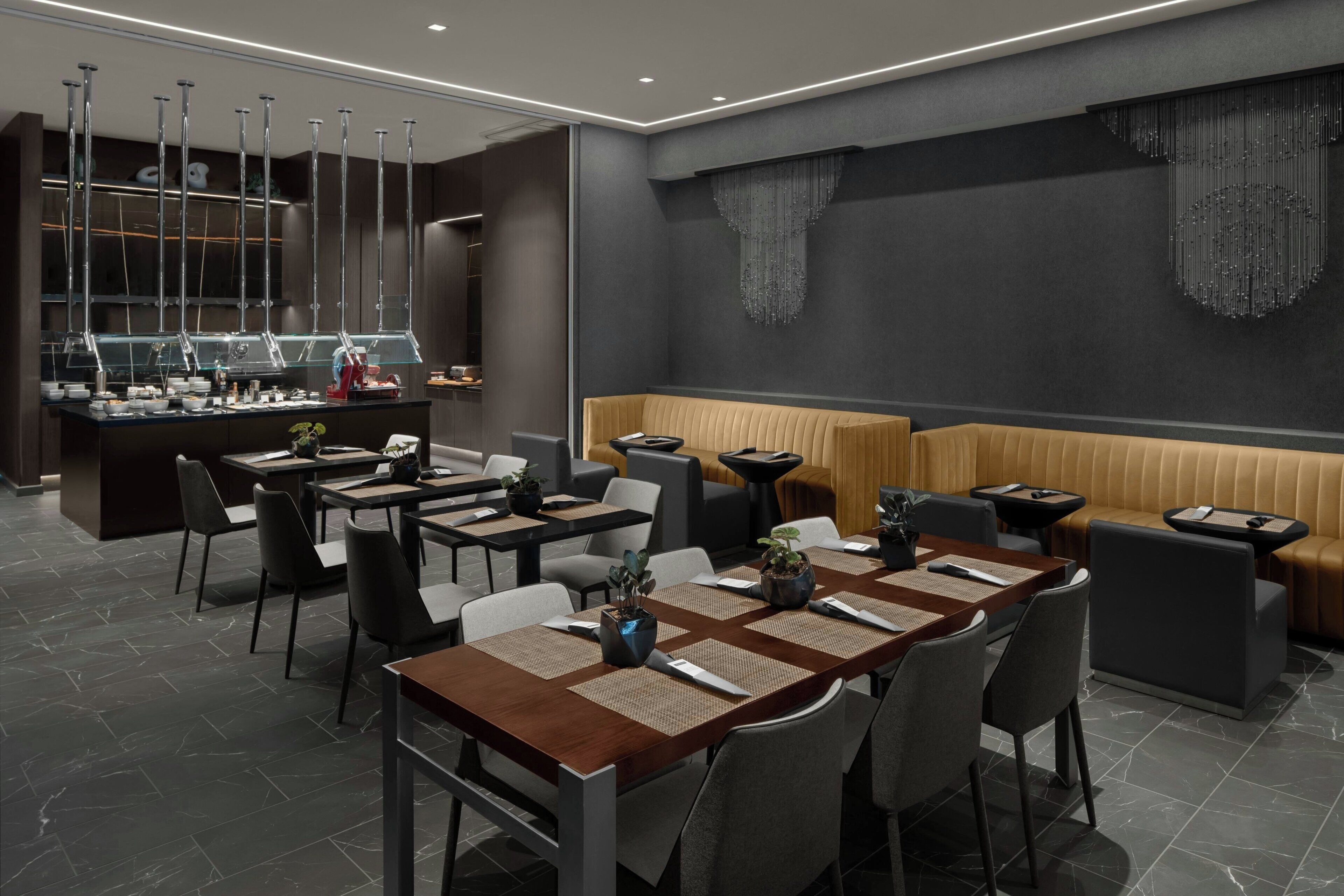 A modern restaurant with a long dining table, cushioned seating, and a bar area.