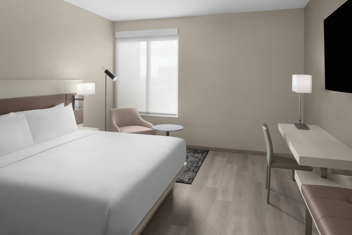 Ett modernt hotellrum med en stor säng, ett skrivbord, en stol och ett litet bord.