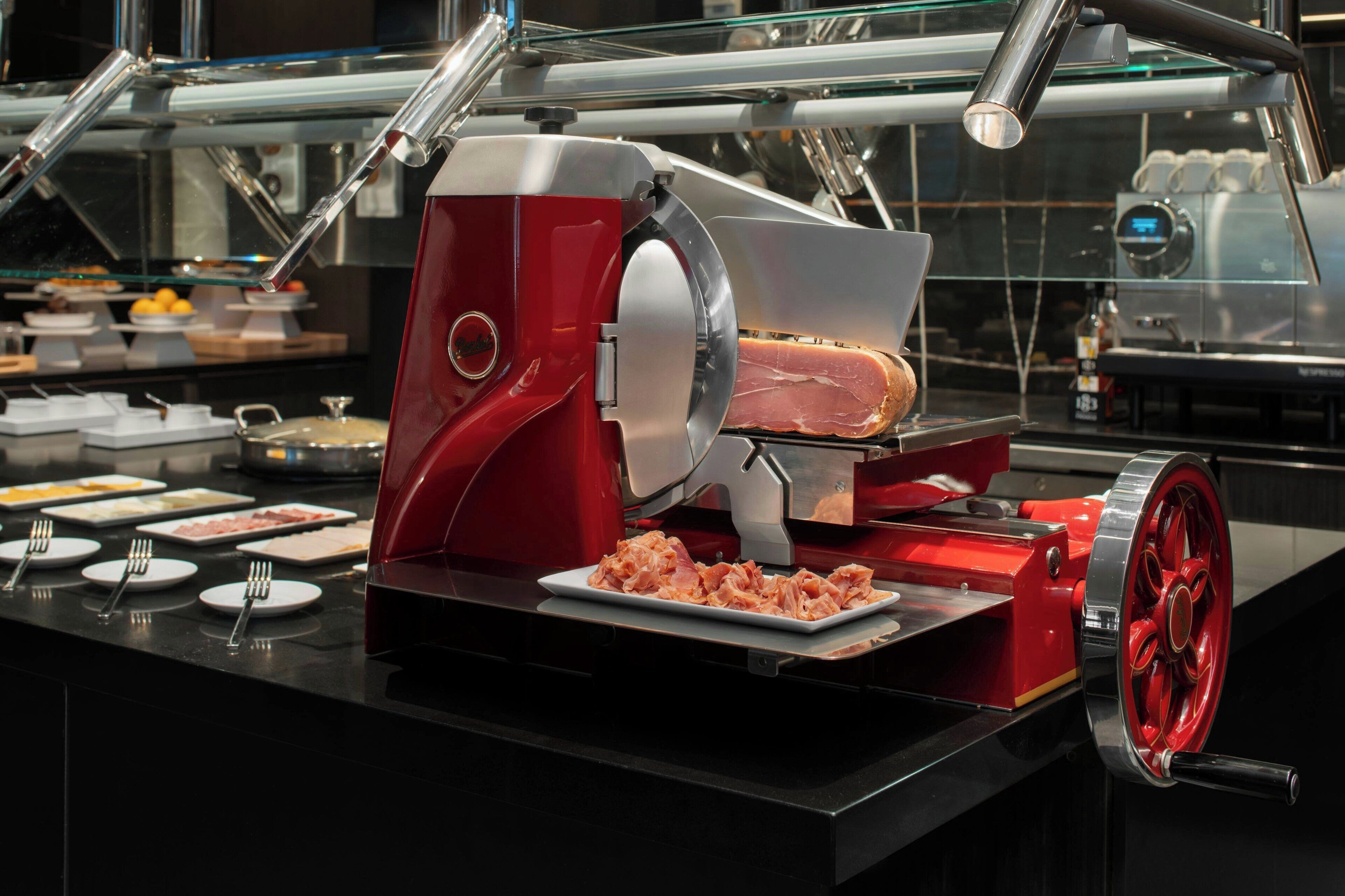 A buffet setup with a meat slicer, serving trays, and utensils.