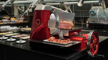 A buffet setup with a meat slicer, serving trays, and utensils.