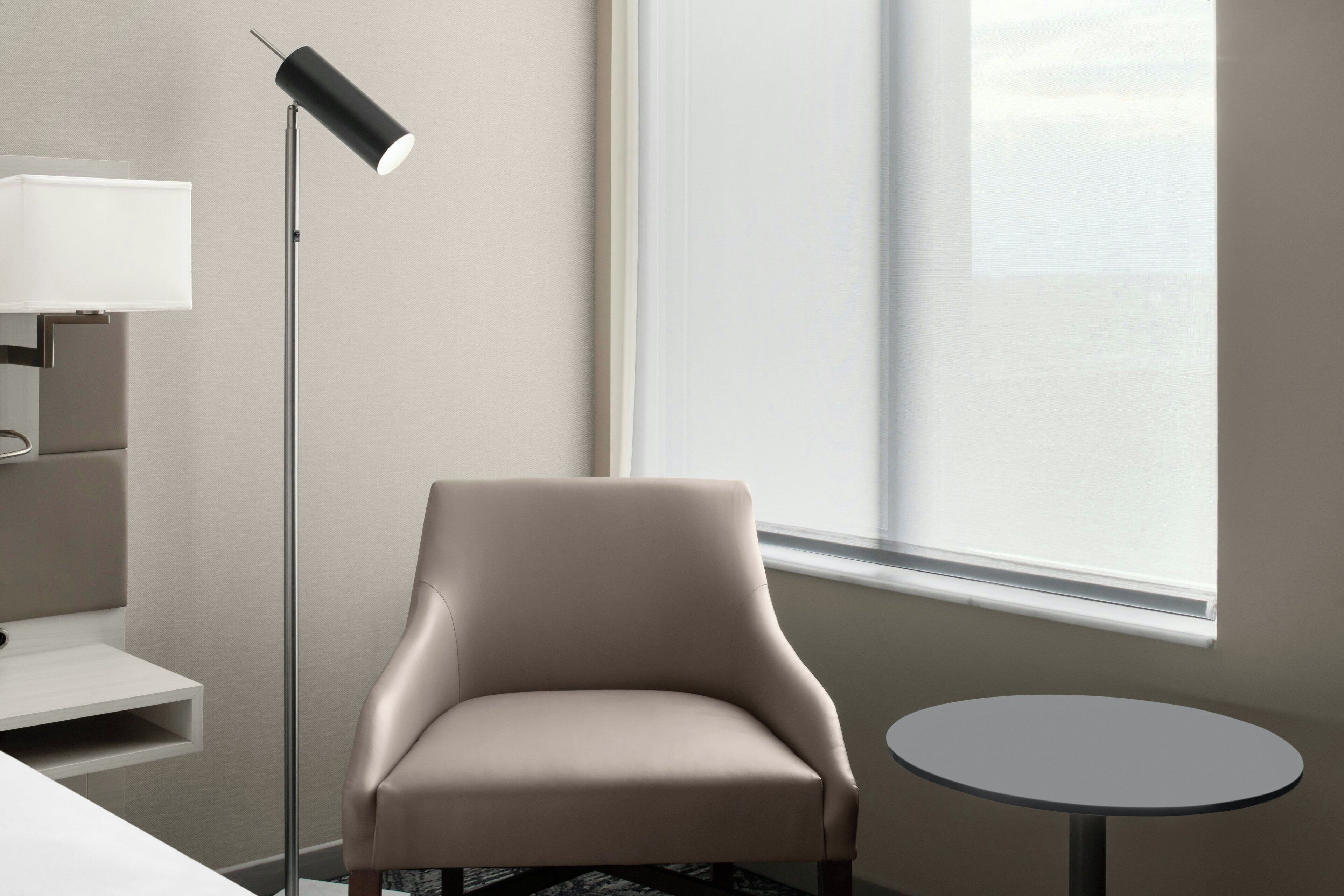 A modern room with a beige armchair, a small round table, a floor lamp, and a window with a view.
