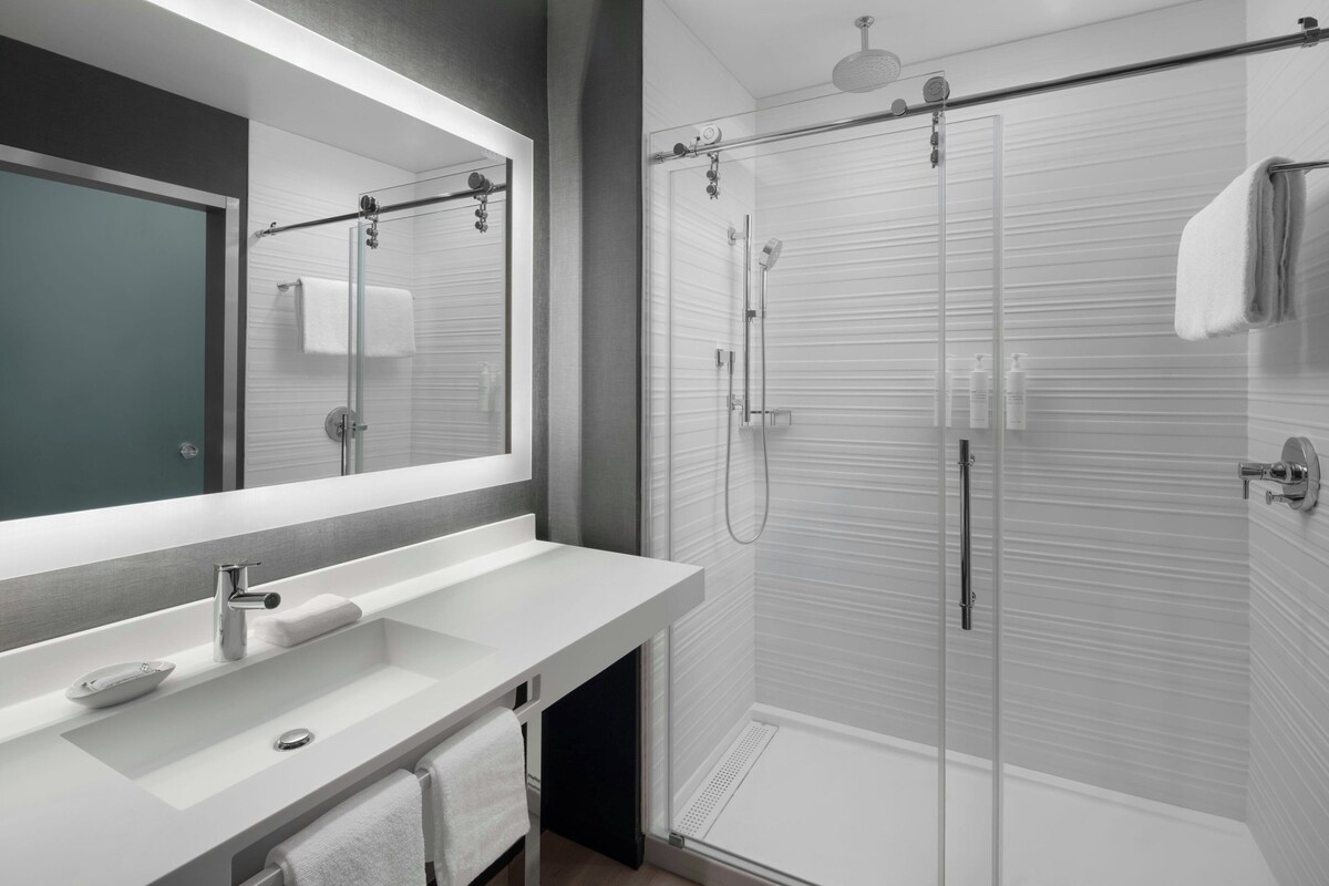 Een moderne badkamer met een grote spiegel, een witte wastafel en een douchecabine met glazen wanden.