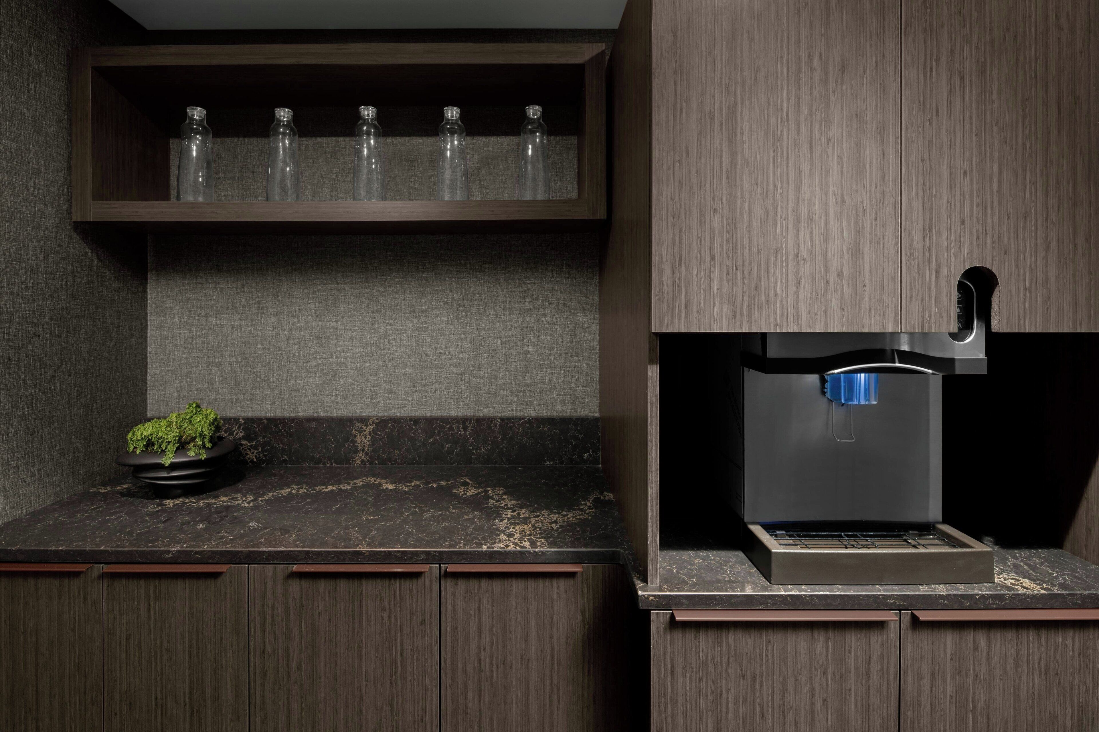 Una cocina con armarios de madera oscura, encimera de mármol y cafetera integrada.