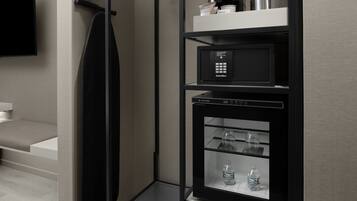 Ein modernes Hotelzimmer mit integriertem, schwarzem Minikühlschrank, einem Flachbildfernseher und einer Sitzecke mit einer Bank.