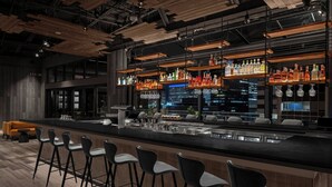 Eine moderne Bar mit mehreren Flaschenregalen, einer Theke und einigen schwarzen Barhocker.