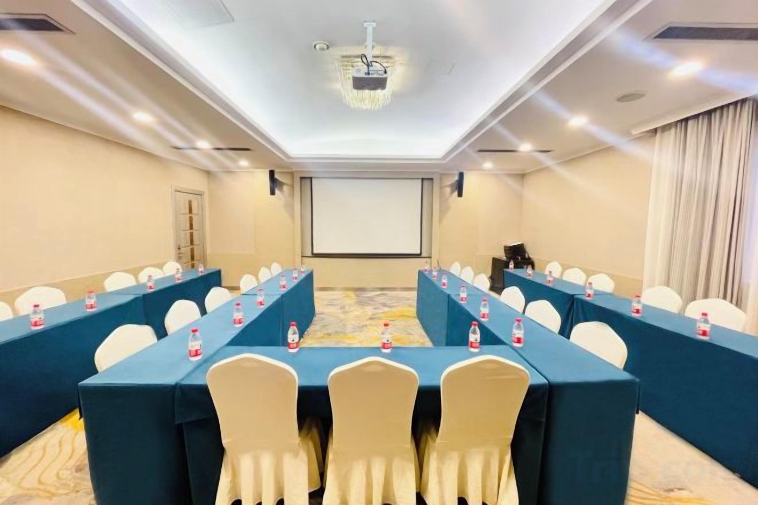 Uma sala de conferências com mesas grandes, cadeiras e uma tela de projeção.