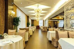 A hotel dining area with round tables, chandeliers, and a long corridor.