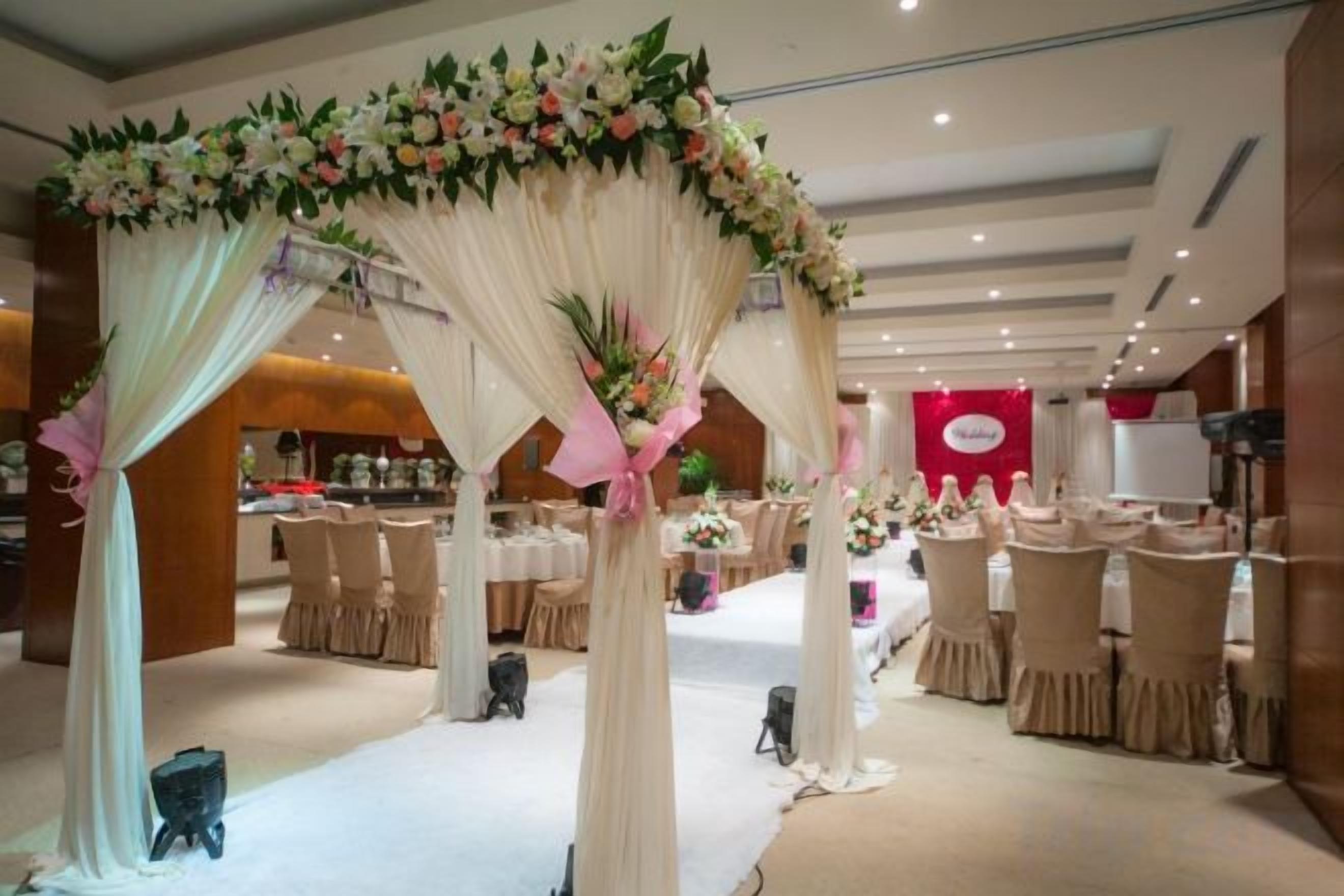 A banquet hall with round tables and chairs, a floral archway, and a red banner in the background.