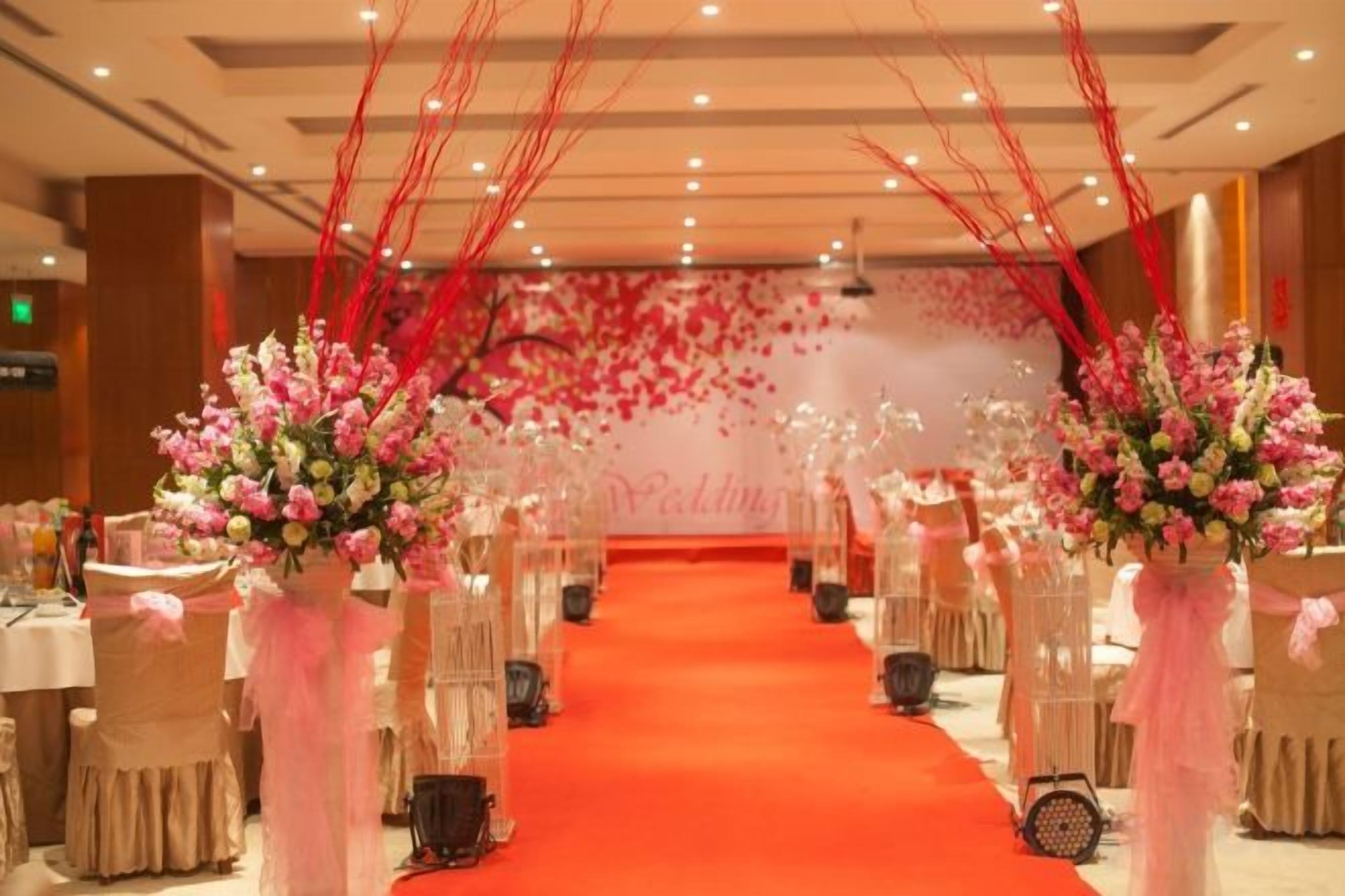 Salão de banquetes com carpete vermelho, mesas redondas e arranjos florais.