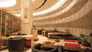 Un interior moderno con paredes curvas, muebles de madera y un pilar central con obras de arte.
