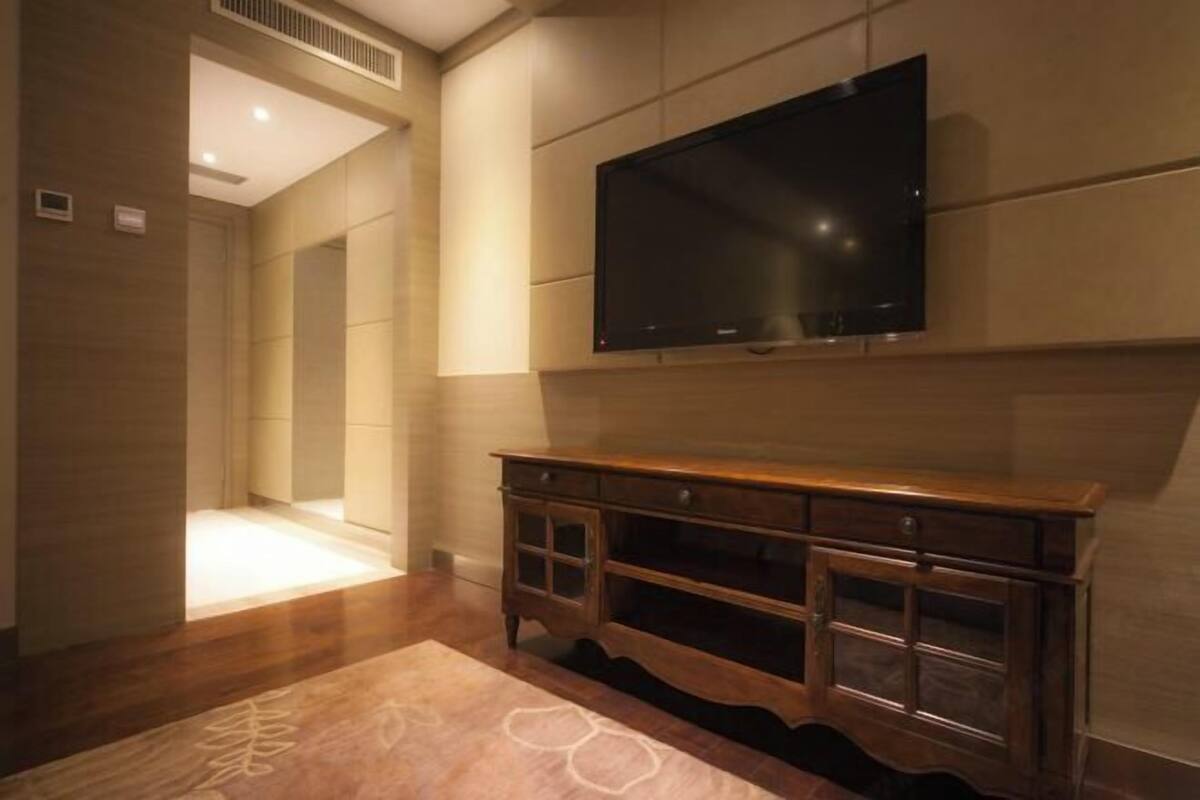 Quarto de hotel moderno com uma televisão de tela grande na parede, um console de madeira com gavetas e um tapete estampado no chão.