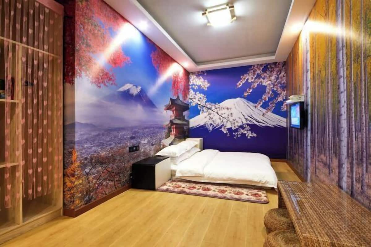 Une chambre avec une grande fresque représentant un paysage montagneux et des fleurs de cerisier, un lit avec du linge de maison blanc, un banc en bois et une petite table.