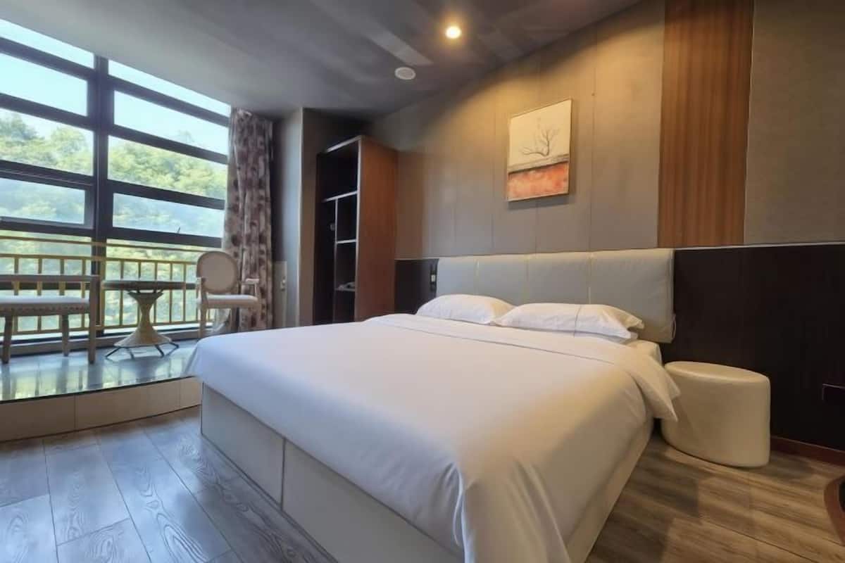 Une chambre d’hôtel moderne avec un grand lit, une table de chevet, une chaise, une fenêtre donnant sur un beau paysage et un tableau au mur.