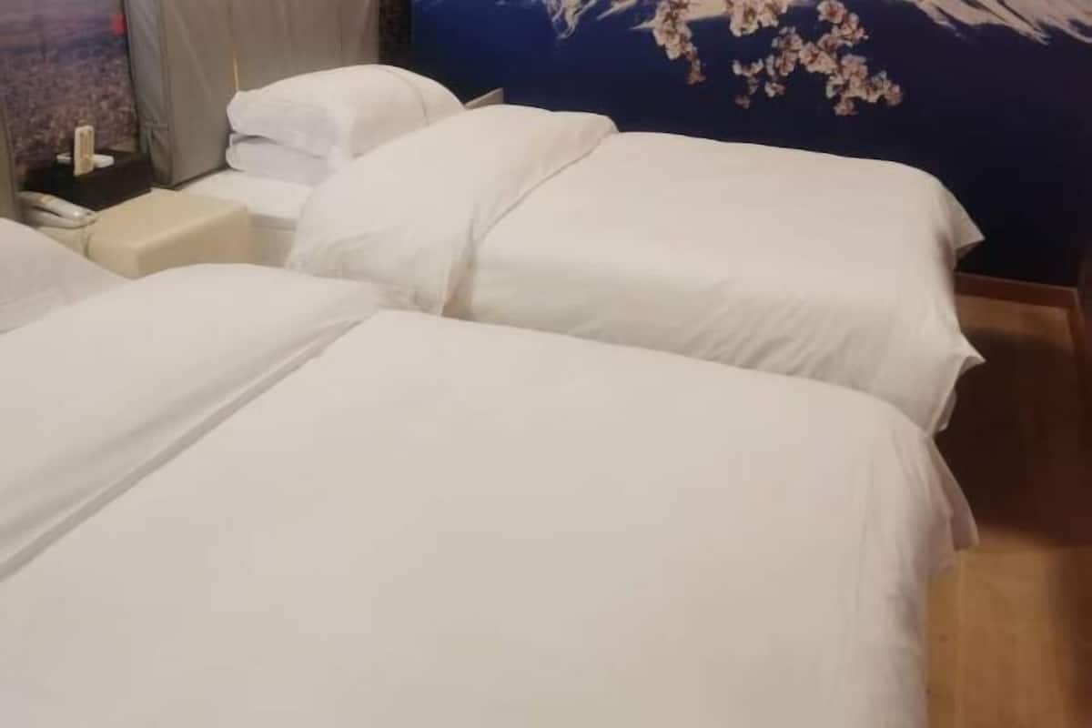 Une chambre d’hôtel avec deux lits, une table de chevet et un mur orné d’un motif floral.