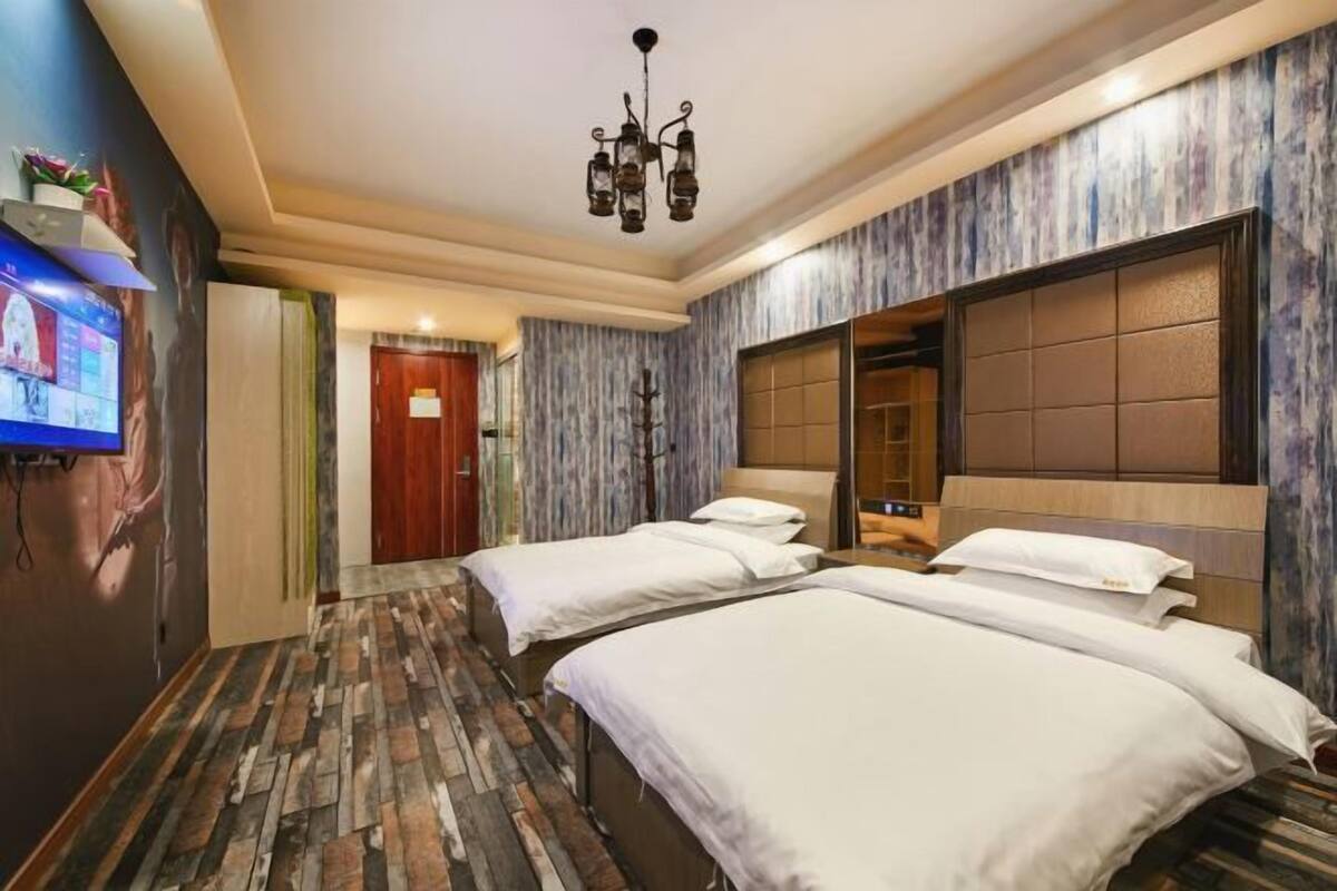 Une chambre d’hôtel avec deux lits, un lustre, une télévision et un mur décoré de motifs.
