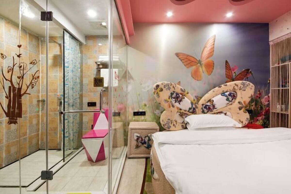 Une chambre d’hôtel dotée d’une douche en verre, d’un lit agrémenté d’oreillers à motifs floraux et d’une fresque représentant des papillons et des fleurs.