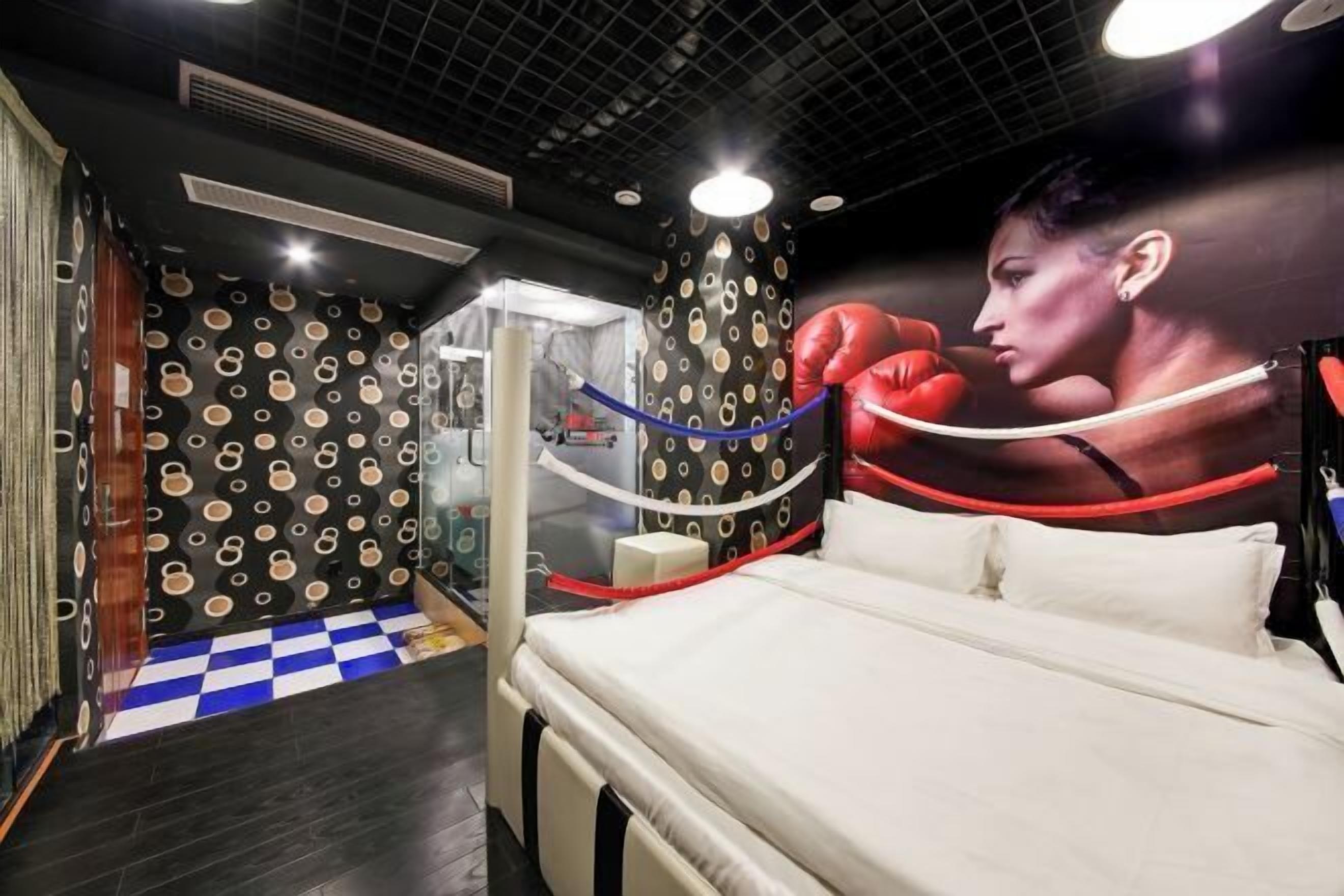 Une chambre d’hôtel avec un lit, un sol à carreaux, une fresque murale sur le thème de la boxe et un mur à motifs.